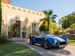 A blue convertible car parked in front of a building with a Mediterranean architectural style, including arches and a stucco facade.