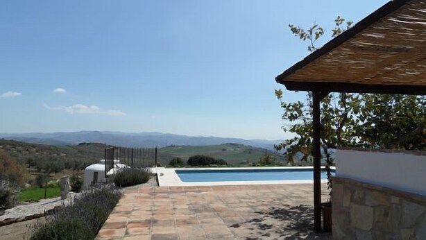 Un espace piscine agrémenté d’une terrasse en pierre, d’une pergola et offrant une vue sur les collines lointaines.