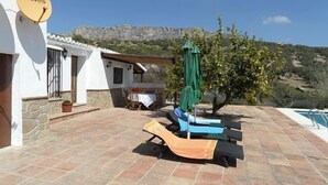 Une terrasse avec une piscine, une table entourée de chaises et un parasol vert.