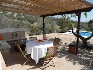 An outdoor patio with a table set for two, surrounded by wooden chairs, a cushioned bench, and a small table with a fruit bowl. - Casa El Trigal for 4 people (Antequera)
