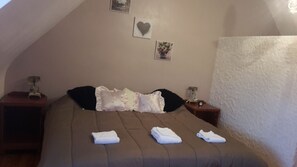 A bedroom with a sloped ceiling, a bed with pillows and a blanket, two bedside tables with lamps, and a wall with a heart-shaped decoration and a framed picture. - SPACIOUS RENTAL FOR 10/12 PERS: 2 EQUIPPED KITCHENS; GARDEN CLOS AND VERANDA (Primelin)