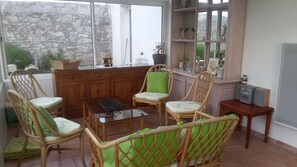 A cozy room with wicker furniture, a wooden cabinet, and a window with a stone wall view. - SPACIOUS RENTAL FOR 10/12 PERS: 2 EQUIPPED KITCHENS; GARDEN CLOS AND VERANDA (Primelin)