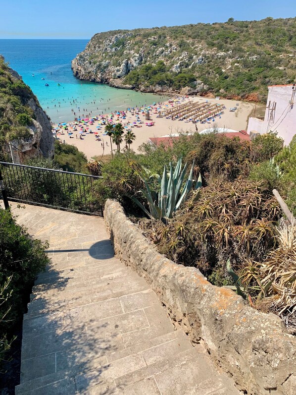A coastal view with a beach, a staircase leading down, and a rocky hillside. - Apartment with dream view in Cala en Porter (Self check-in/out) (Cala 'n Porter)