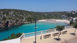 Vista costera con un litoral rocoso, una playa con sombrillas y un paseo marítimo con bancos.