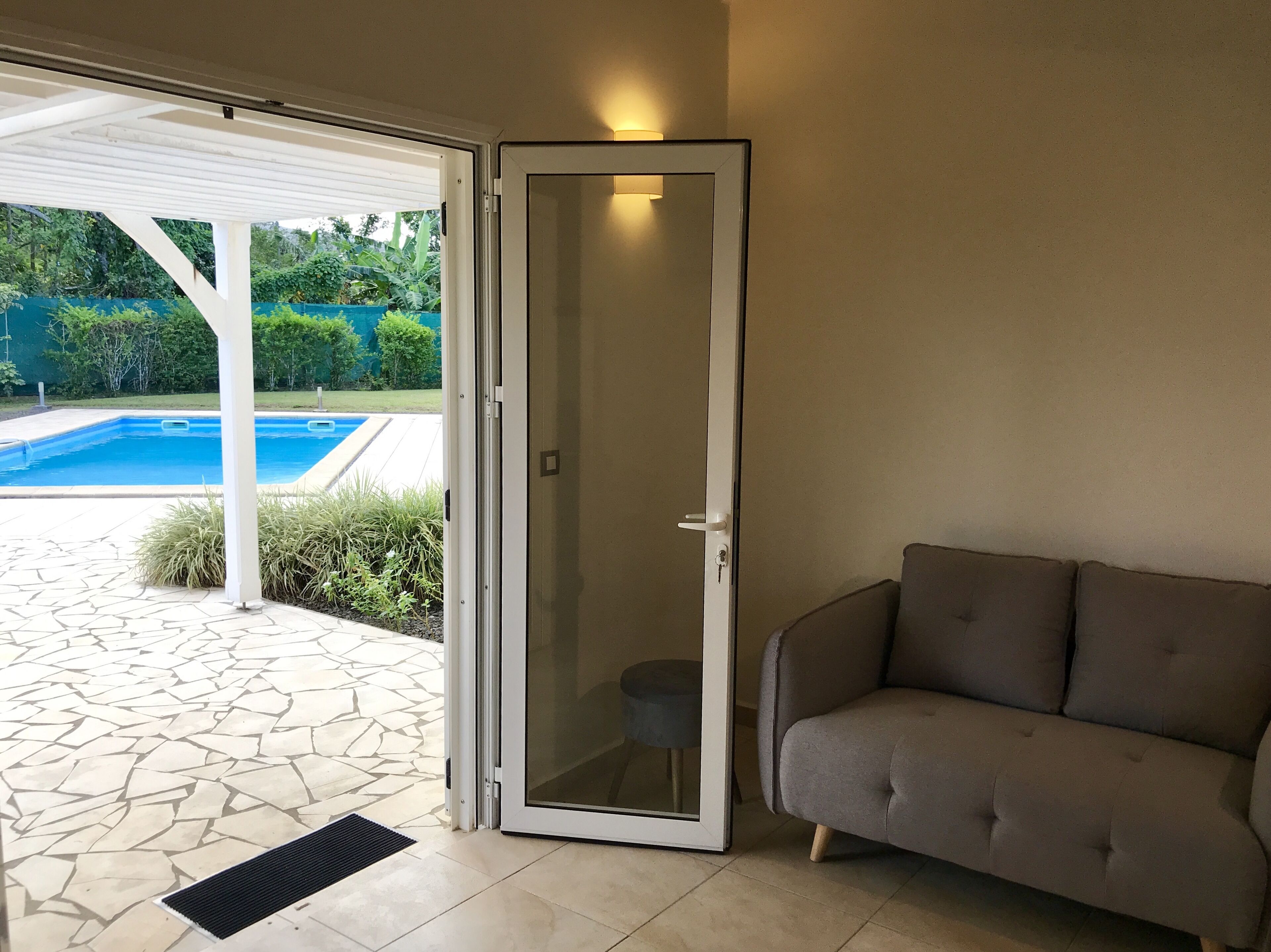 A room with a sliding glass door leading to a pool area, a grey sofa, and a tiled floor.