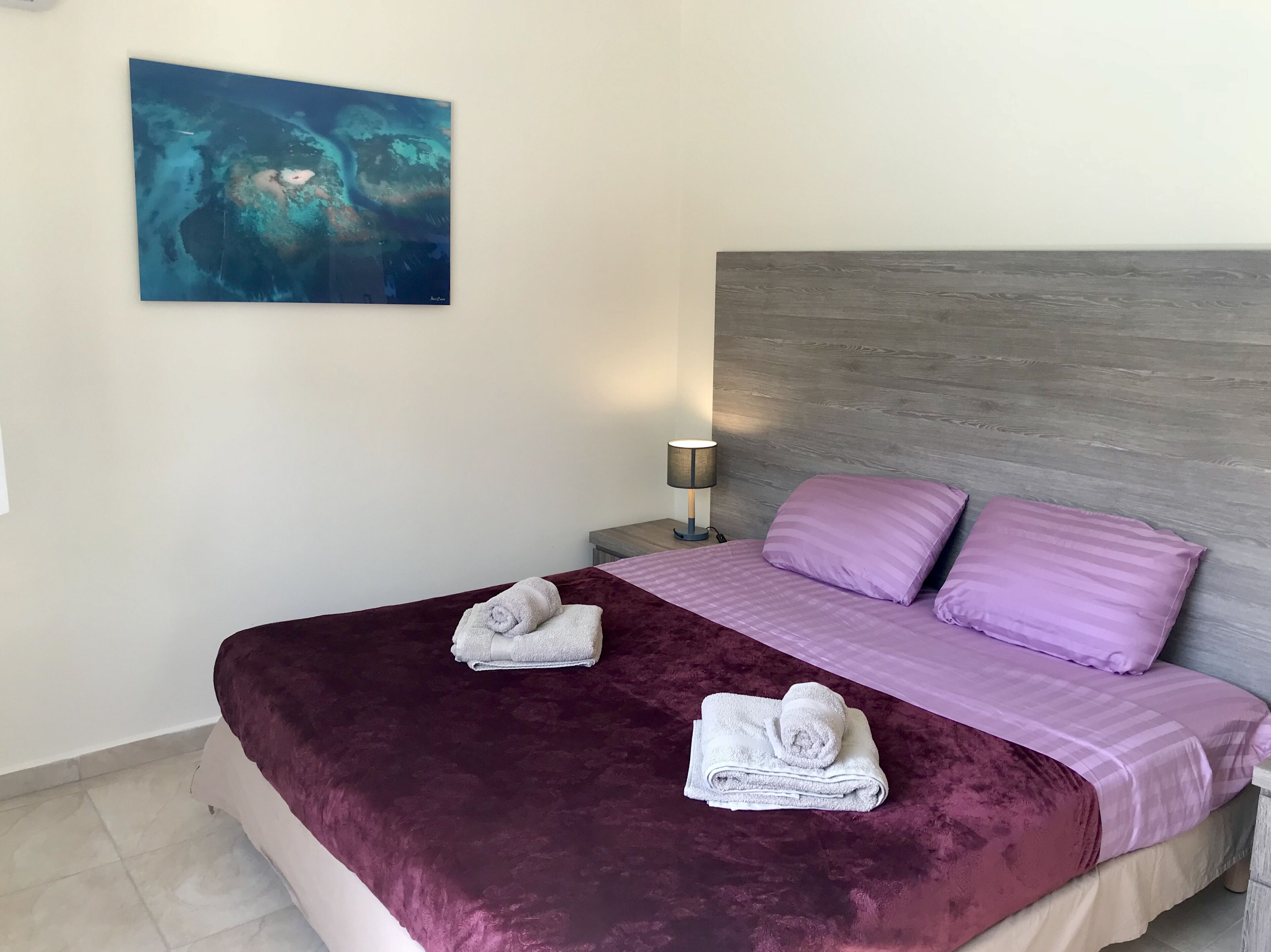 Ein Hotelzimmer mit einem großen Bett, einem Kopfteil, einem Nachttisch mit Lampe und einem Gemälde an der Wand.