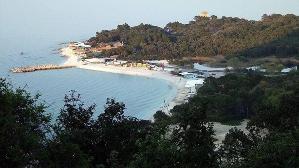 Eine Küstenlandschaft mit Strand, einem kleinen Steg und einem Hügel mit einem Gebäude auf der Spitze.