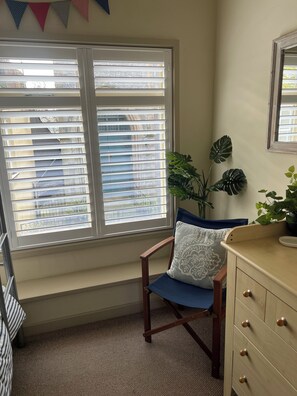 A room with a window, a chair, a plant, and a dresser.
