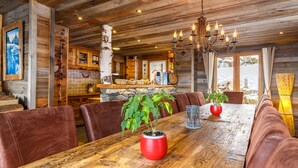 Un interior rústico de madera con una mesa de comedor, asientos de cuero, una araña y vistas al exterior.