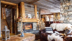 Un interior rústico con chimenea de piedra, vigas de madera y un sofá de cuero con cojines de piel.