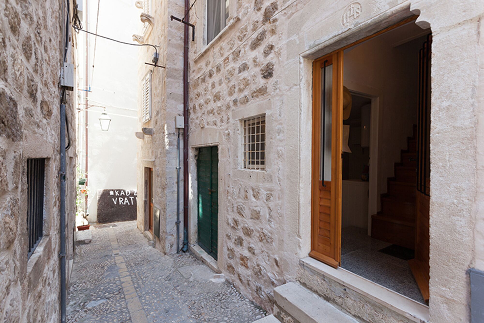 Una calle estrecha con edificios de piedra, una puerta visible y una escalera que lleva al interior.