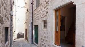A narrow street with stone buildings, a visible door, and a staircase leading inside.