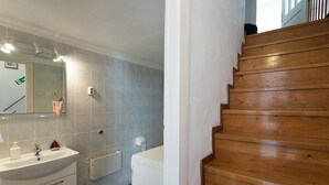 A bathroom with a sink, mirror, and toilet. There is a wooden staircase to the right.