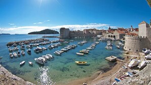 A coastal town with a historic fort, clear waters, and numerous boats docked at the harbor.