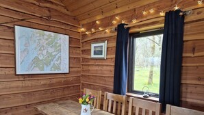 A wooden cabin interior with a wooden bench, a map on the wall, and a window with curtains.
