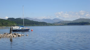 A calm lake with a boat docked on the shore, surrounded by mountains and clear skies.