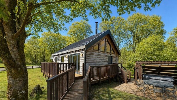 A rustic cabin with a wooden deck, a covered outdoor seating area, and a chimney.