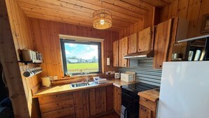 A wooden cabin kitchen with a window, wooden cabinets, a sink, a stove, and a refrigerator.