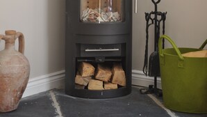 A wood-burning stove with a glass door, a metal handle, and a green bucket nearby. - Cottage In Prestleigh, Somerset, England (Prestleigh)