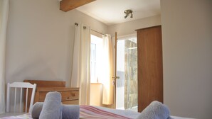 A bedroom with a bed, a wooden dresser, a white chair, and a bathroom visible through an open door. - Cottage In Prestleigh, Somerset, England (Prestleigh)