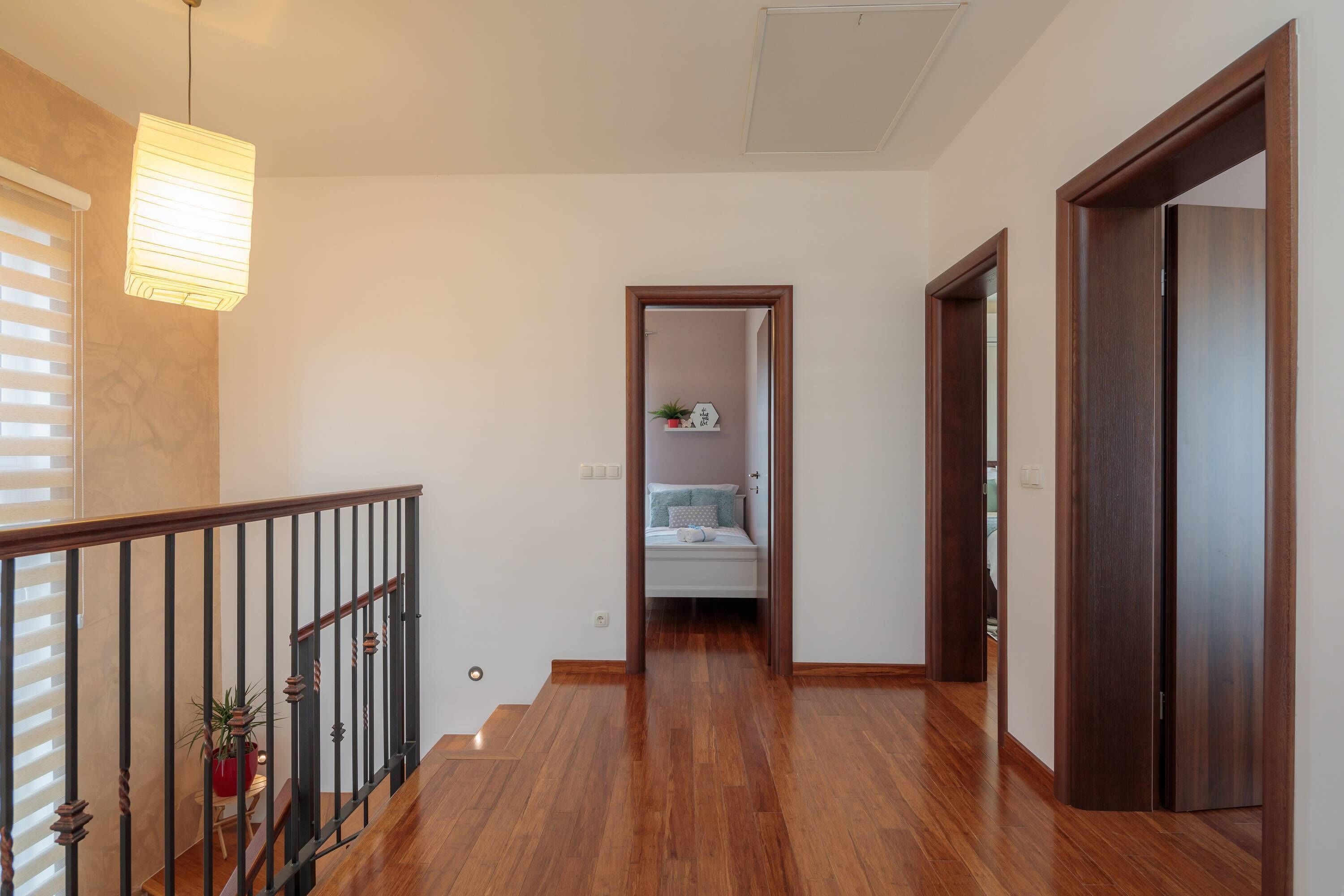 A hallway with wooden flooring, a staircase, and a bed in the background.