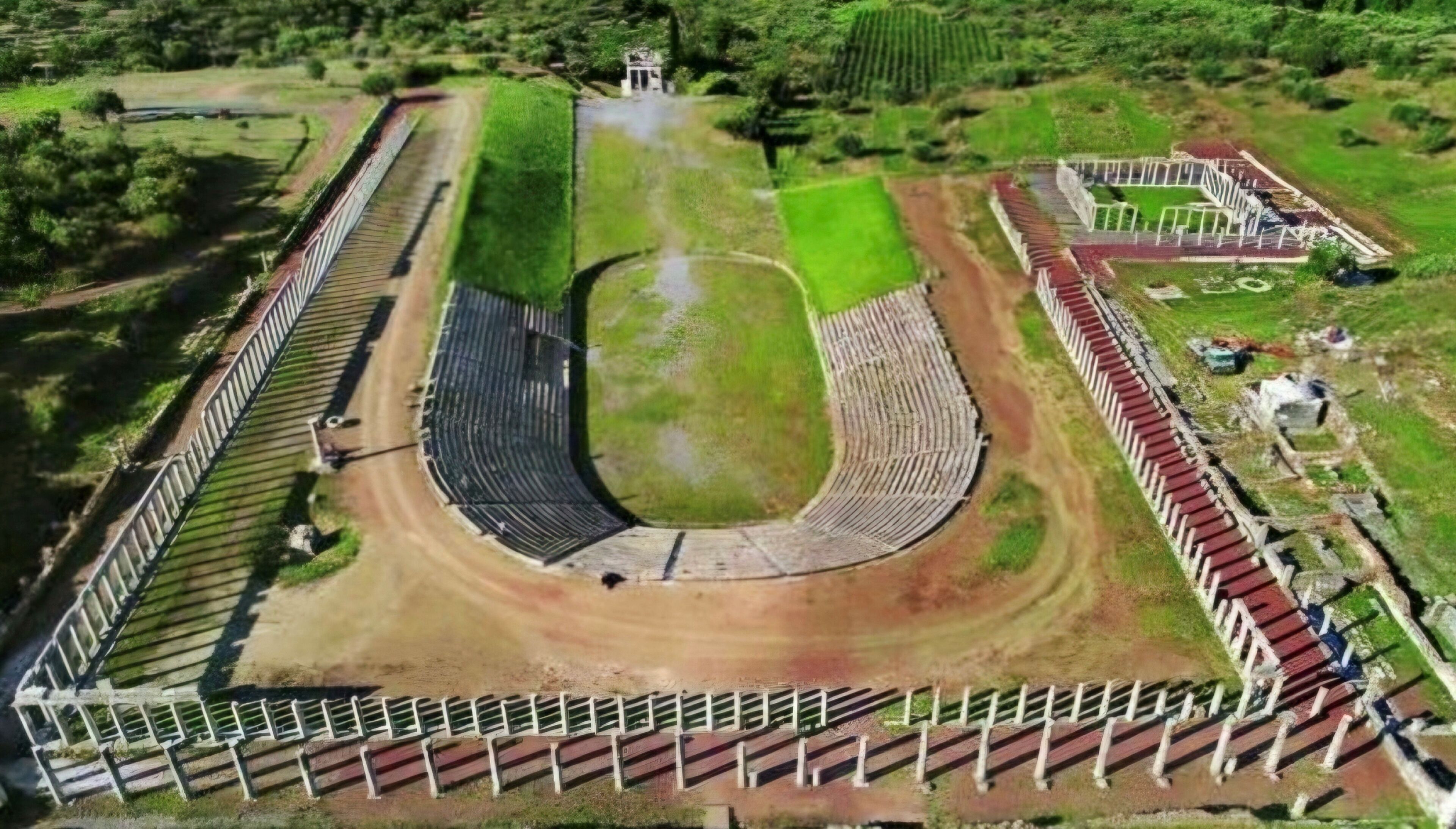 Vista aérea de un estadio con una pista central, gradas para espectadores y zonas verdes circundantes.