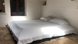 Una cama individual con cubrecama blanco en una habitación con suelo de baldosas y ventana con marco de madera.