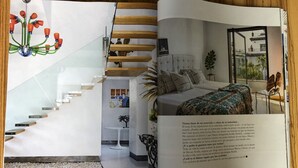 Un intérieur moderne avec un escalier, un lit recouvert d’une couvre-lit à motifs et une vue sur le paysage urbain par la fenêtre.