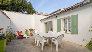 A patio with a white table and chairs, surrounded by potted plants and a colorful chair.