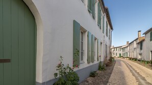A narrow cobblestone street lined with traditional buildings featuring green shutters and white walls.