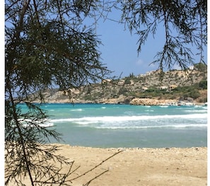 A coastal landscape with clear turquoise waters, rocky terrain, and buildings on a hillside.