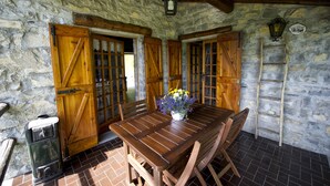 A rustic stone-walled room with wooden doors, a table with chairs, and a small heater. - BETWEEN THE FOREST AND THE LAKE (Schignano)