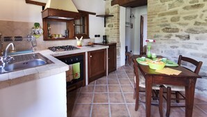 Eine rustikale Küche mit Steinwand, Holzbalken, Spüle, Herd und einem Essbereich mit Tisch und Stühlen.