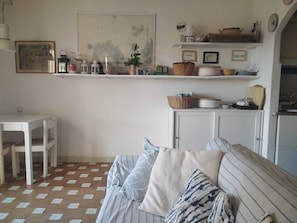 Una sala de estar con sofá, mesa y aparador. Hay repisas sobre el aparador con varios objetos.