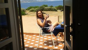 Una persona sentada en una silla cerca de una puerta, con vista al mar y las colinas al fondo.