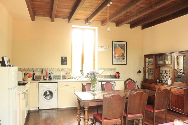 A kitchen with a washing machine, a dining table with chairs, and a cabinet with glass doors. - Farmhouse With Private Heated Pool (June to Sept) (Gibourne)