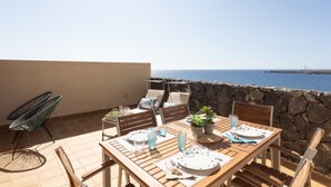 A wooden table set with plates, glasses, and a potted plant on a balcony with a stone wall and a view of the sea. - Total Relax Apartment (Porís de Abona ( Arico ))