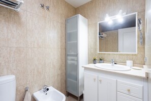 A modern bathroom with a white sink, vanity, and cabinet, a bidet, and a large mirror with lights. - Total Relax Apartment (Porís de Abona ( Arico ))