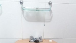 Un baño con un lavamanos color crema, un estante de vidrio encima y un inodoro a la derecha.