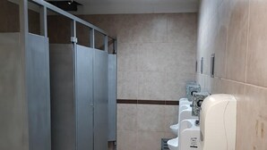 Baño público con múltiples cabinas, un secador de manos y piso de baldosas.