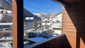 Une vue depuis une fenêtre donnant sur un village de montagne enneigé, où l’on aperçoit un autobus et un télésiège.