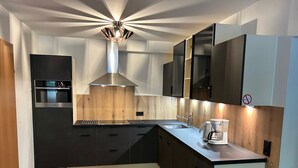 Une cuisine moderne avec des meubles noirs, une hotte en acier inoxydable et un four encastré.
