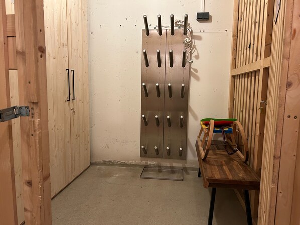 Une pièce avec une porte en bois, un porte-manteau en métal et un banc en bois sur lequel sont disposés divers objets colorés.