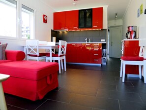 A modern kitchen with red cabinets, white chairs, and a red ottoman.