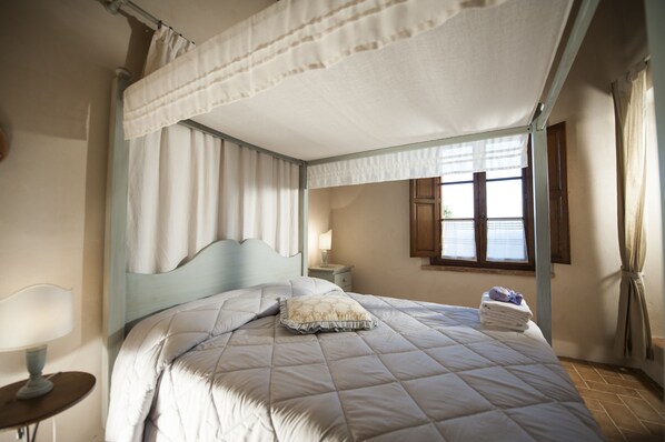 Una cama con dosel y doselado, una mesita de noche con lámpara y una ventana con cortinas.