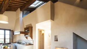 Een ruime woonkamer met een open haard, een bank en een keuken op de achtergrond.