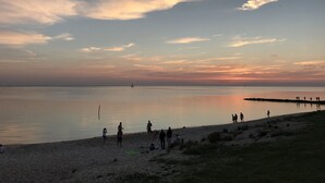 A beach scene with a calm sea, a few people walking, and a sailboat in the distance. - Seaview & Sunset with beautiful views over the IJsselmeer (102) (Stavoren)