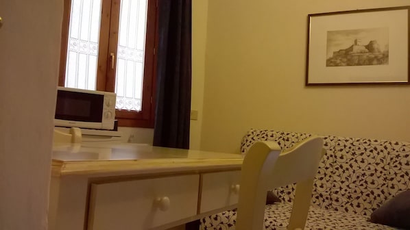 Una habitación con un escritorio de madera, un microondas blanco, un sofá estampado y un cuadro en la pared.