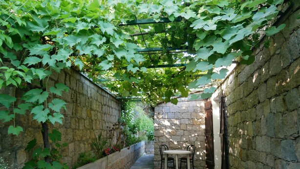 A narrow stone-walled courtyard with a pergola covered in green foliage, a table with chairs, and a stone bench. - Nice house with view (Vero)