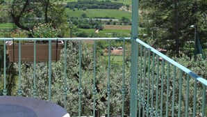 Un balcón con vistas a un paisaje montañoso, baranda de metal y una lámpara colgante.